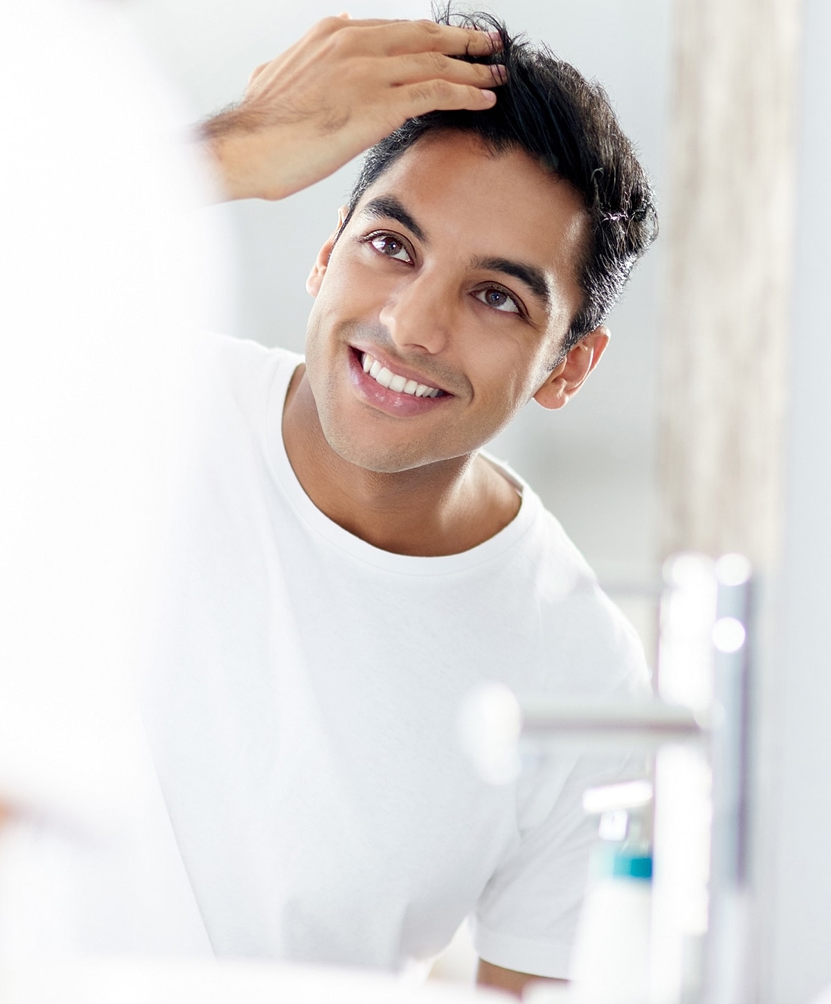 Smiling man styling hair in bathroom mirror.