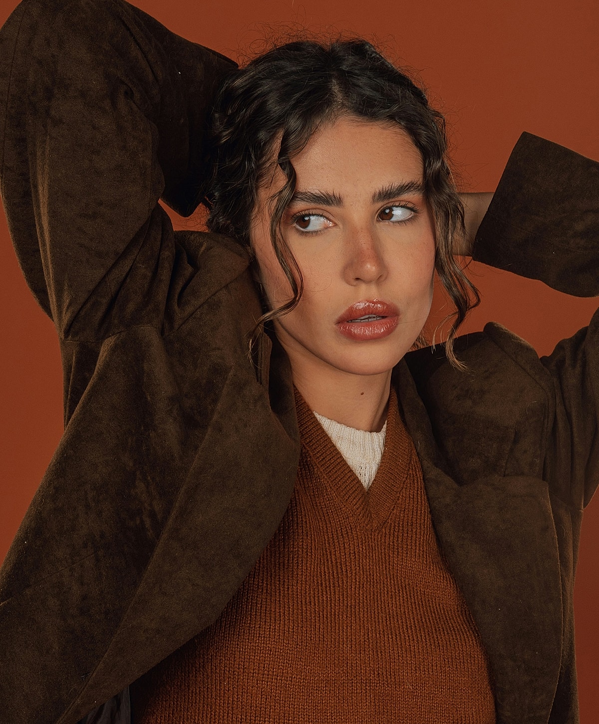 Model in brown outfit against orange backdrop.