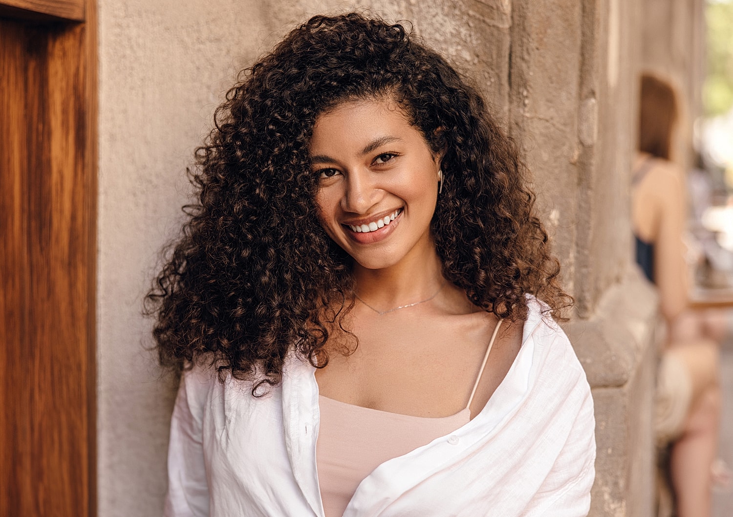 Smiling woman with curly hair against a wall.