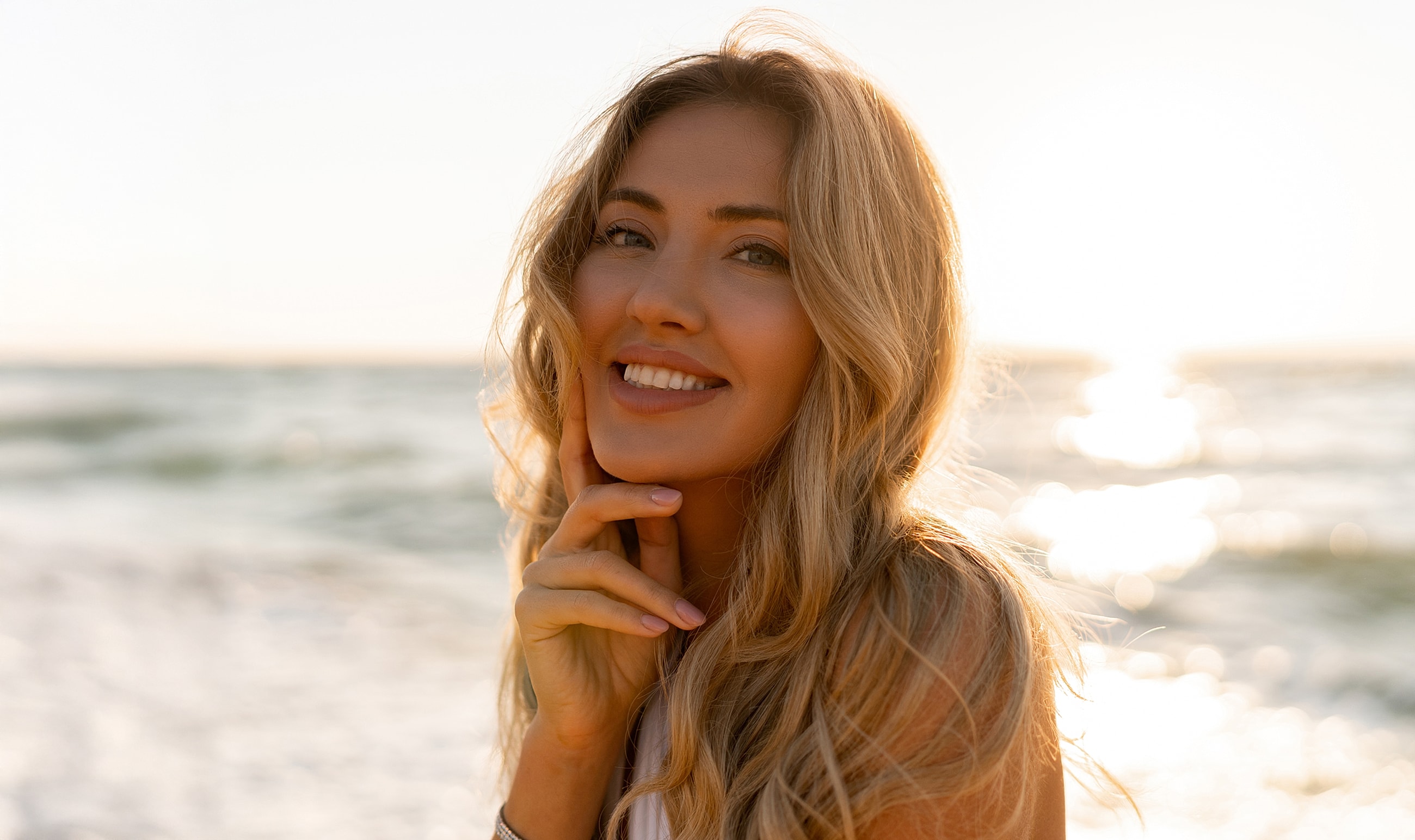 Smiling woman by the ocean at sunset.
