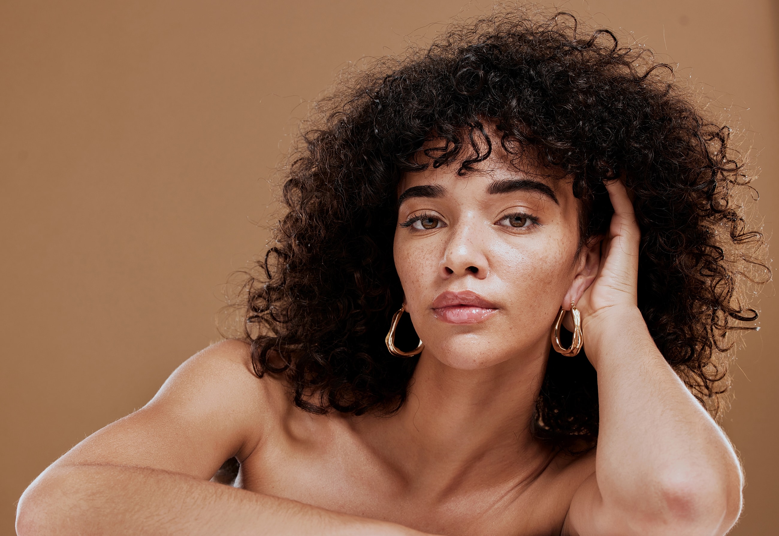 Beverly Hills facial fat grafting model with curly hair and earrings against backdrop.